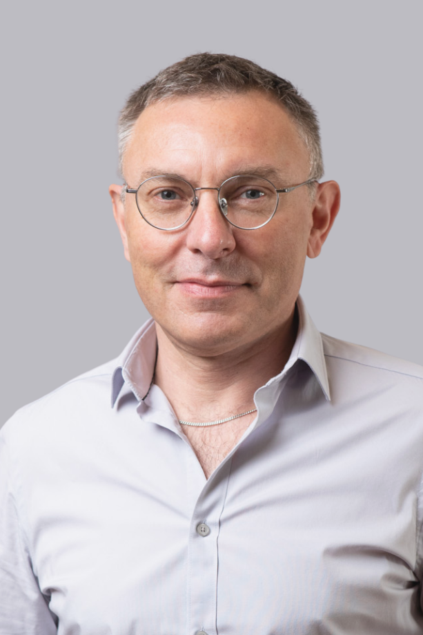 Portrait d'un homme portant des lunettes et une chemise blanche, regardant l'objectif, sur fond neutre.